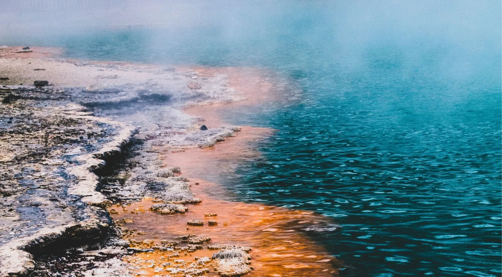 Close view of the boundary between orange mineral crust and deep teal water at the Champagne Pool