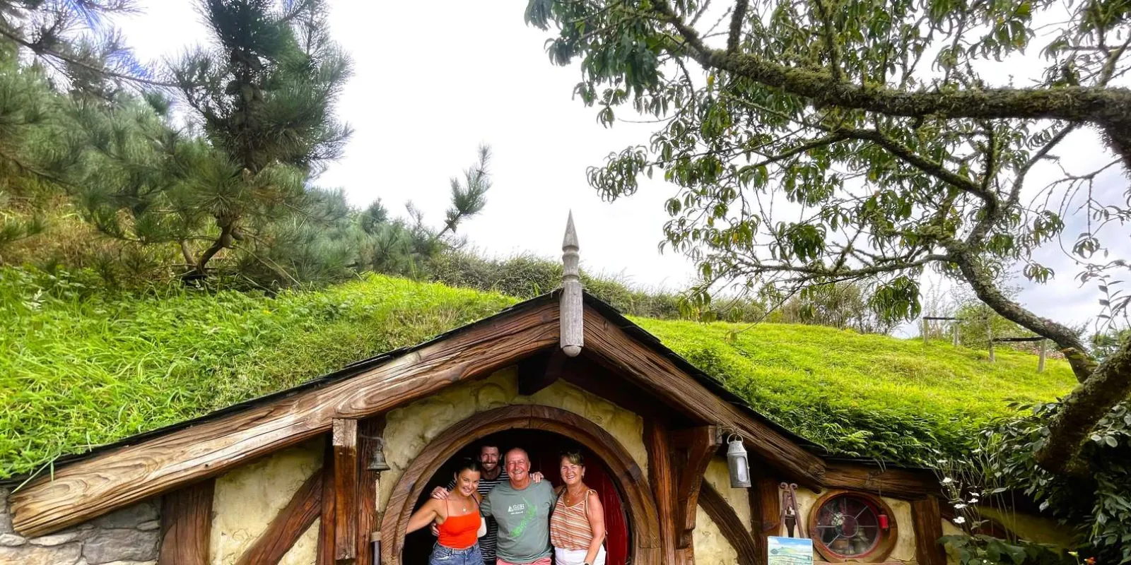 Four travellers standing in the round doorway of a hobbit hole at Hobbiton