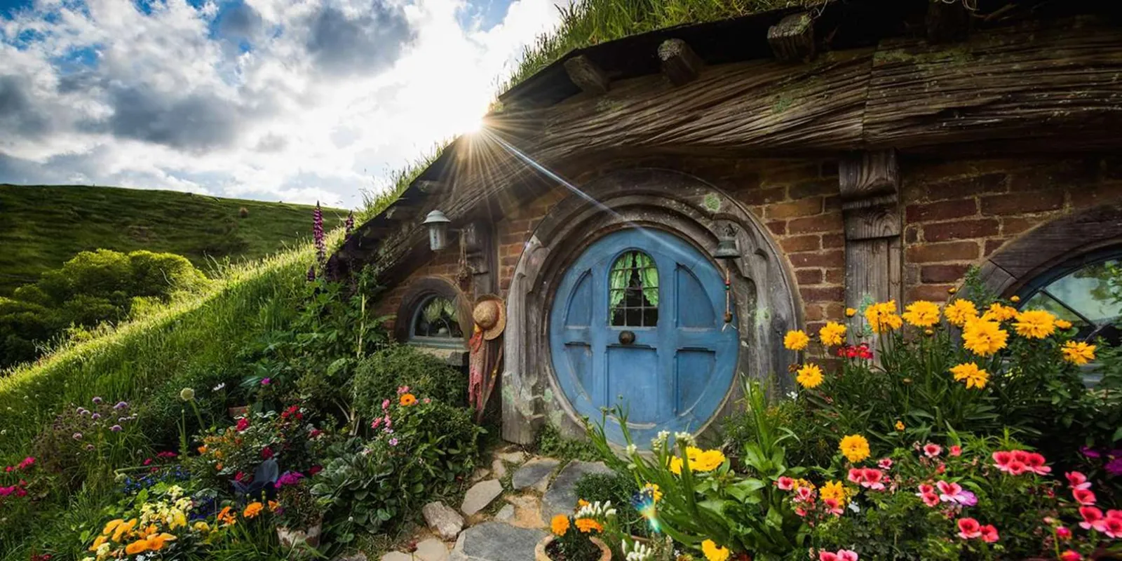 A hobbit hole with a blue round door and flower beds at the Hobbiton Movie Set