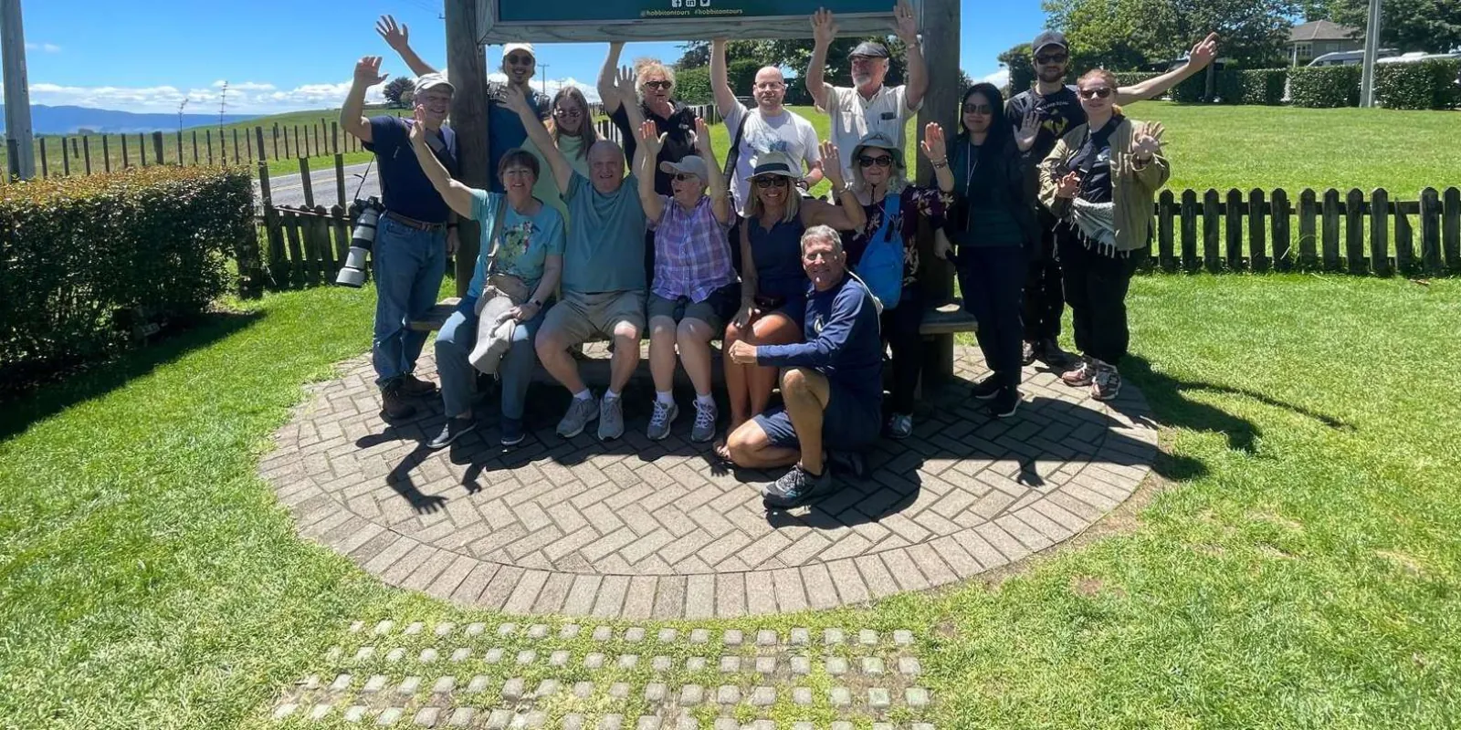 A tour group waving beneath the Hobbiton Movie Set entrance sign