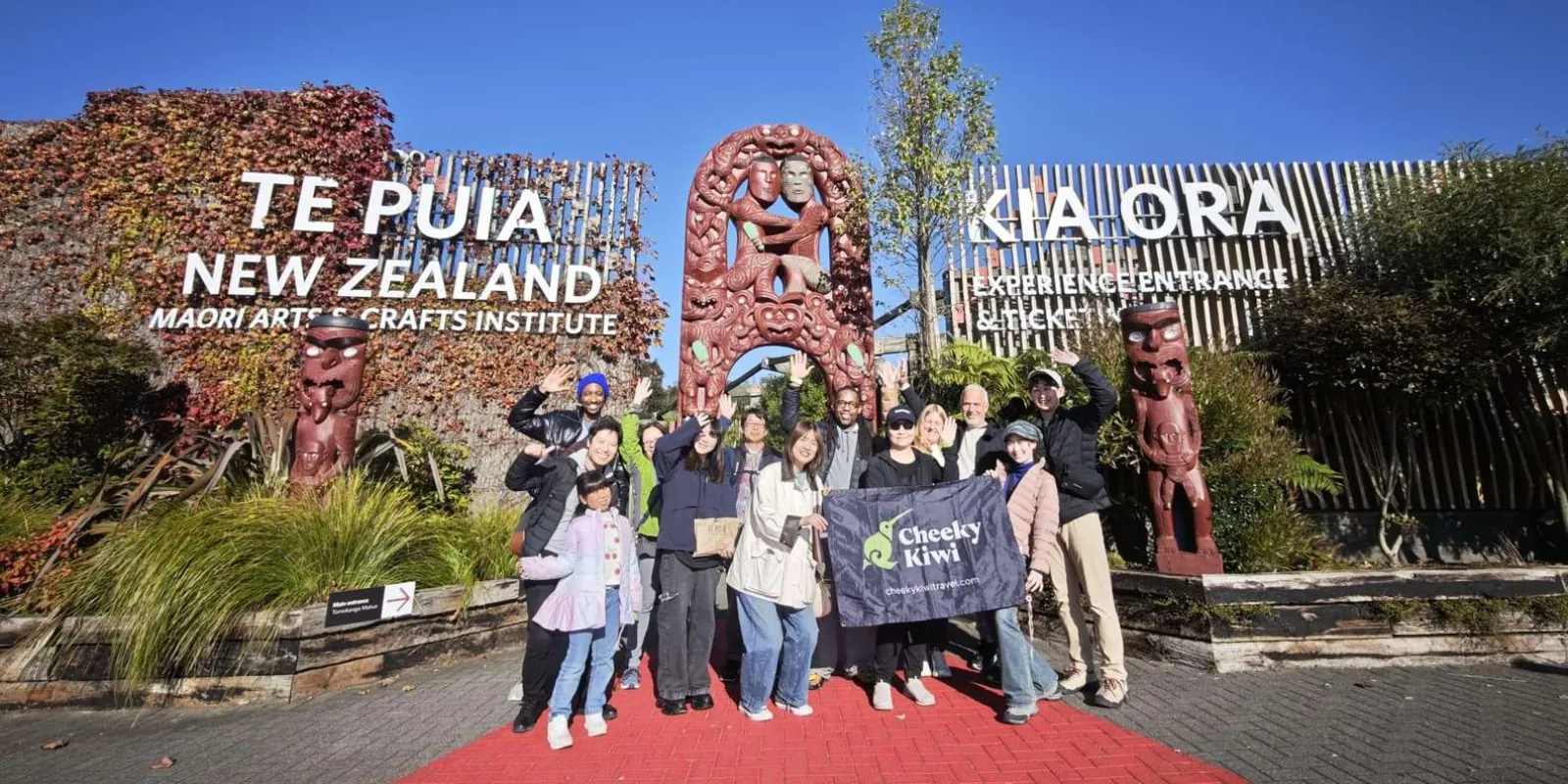 A tour group with their guide's flag at the carved entrance gateway to Te Puia, Rotorua