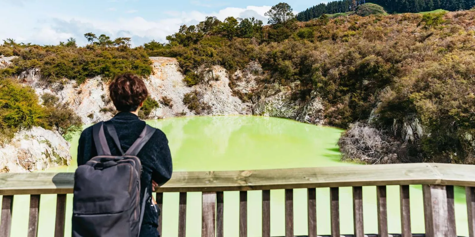 A visitor at the Devil's Bath viewing rail, looking out over the lime-green crater lake